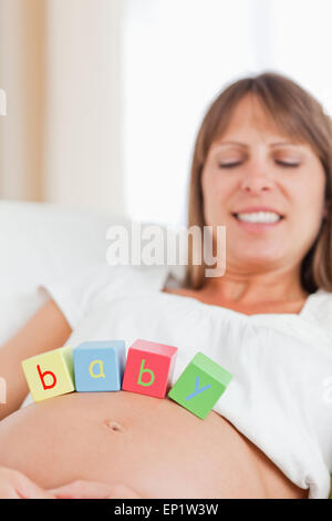 Attraktive schwangere Frau auf einem Sofa liegend mit Holzklötzen spielen Stockfoto