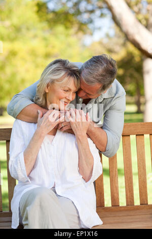 Älterer Mann umarmt seine Frau, die auf der Bank Stockfoto