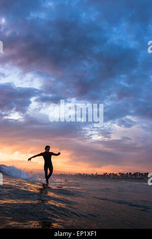 Silhouette eines Surfers, der bei Sonnenuntergang an der Nase seines Longboards läuft, Huntington Beach, Orange County, Kalifornien, USA Stockfoto