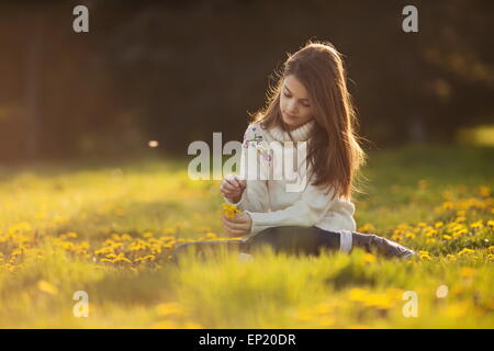 Mädchen sitzen in einem Feld von Löwenzahn Blumen pflücken Stockfoto