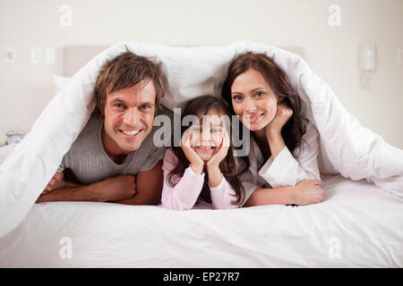 Lächelnden Eltern liegen unter einer Bettdecke mit ihrer Tochter Stockfoto