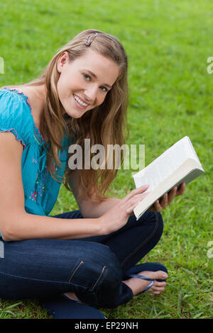 Junge lächelnde Frau in die Kamera schaut, beim Lesen eines Buches Stockfoto