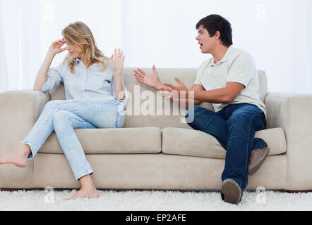 Ein Mann hat einen Streit mit seiner Freundin beim Sitzen auf einer couch Stockfoto