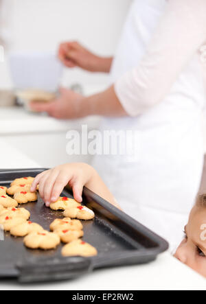 Niedliche kleine Mädchen unter Cookies, während ihre Mutter kocht Stockfoto