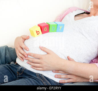 Nahaufnahme einer schwangeren Frau mit Baby auf dem Bauch und ihres Ehemannes auf einem Sofa liegend Stockfoto