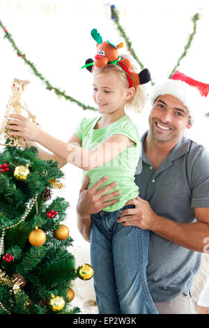Glücklicher Vater seine Tochter, einen Engel auf den Weihnachtsbaum zu helfen Stockfoto