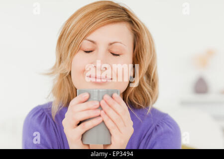 Prety rothaarige Frau halten und riechen eine Tasse Kaffee auf einem Sofa sitzend Stockfoto