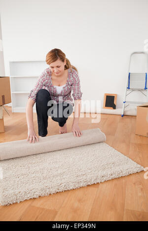 Hübsche Frau, die einen Teppich aufrollen, Umzug vorbereiten Stockfoto