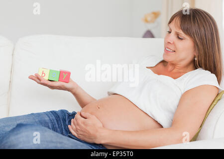 Attraktive schwangere Frau spielen mit Holzklötzen und haben das Wort junge geschrieben auf ihrer Hand Stockfoto