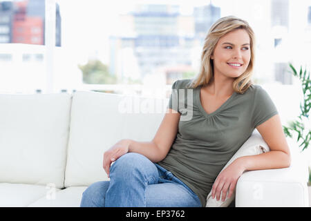 Frau auf Couch sitzen, Lächeln, Beine gefaltet und Blick auf die Seite Stockfoto