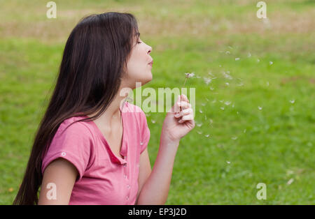 Junge Frau stehend in einem Park während bläst einen Löwenzahn Stockfoto