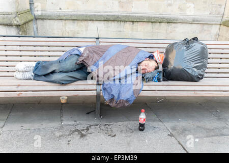 Eine Obdachlosigkeit Person schlafen rau auf einer Bank im Bad Somerset mit einer Tasche von Gegenständen Stockfoto