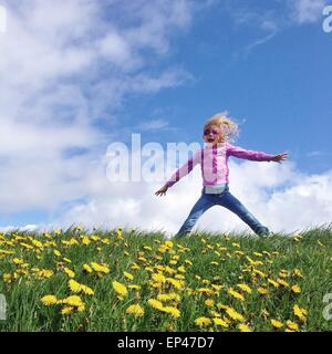 Mädchen springen in einem Feld von Löwenzahn Stockfoto