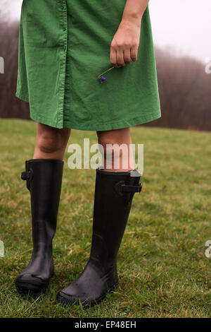 Frau trägt Gummistiefel, die eine violette Blume Stockfoto