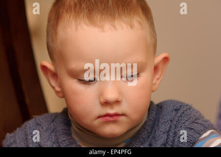 der kleine Junge sitzt auf einem Stuhl und leider schaut Stockfoto