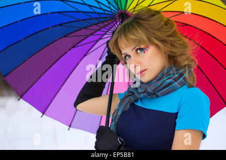 Junge Frau mit mehrfarbigen Regenschirm im Winterwald Stockfoto