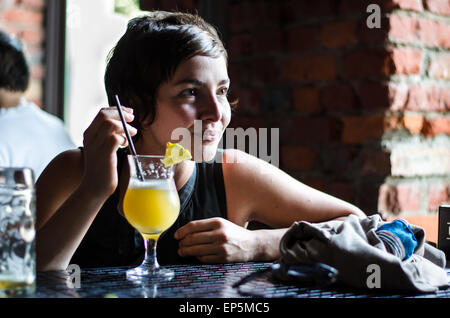 Ein Mädchen in einem roten Kleid sitzen (Aufenthalt) in einem Café mit einem Glas von Pina colada Stockfoto