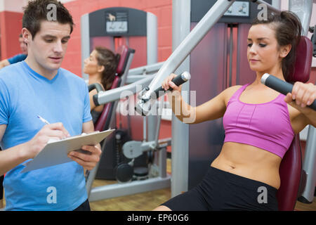 Trainer, die Notizen auf Client auf Gewichte Maschine Stockfoto