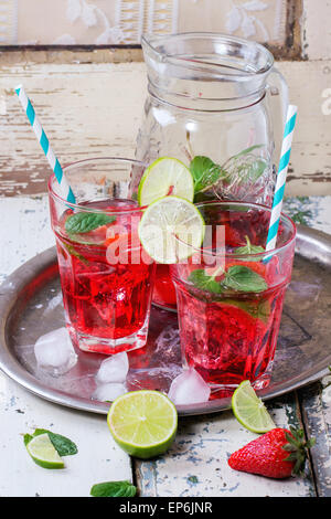 Zwei Gläser mit Retro-cocktail Röhren und Glaskrug mit hausgemachtem Erdbeer Limonade, serviert mit frischen Erdbeeren, Minze, Limette Stockfoto