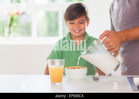 Vater, indem Milch in das Getreide des Sohnes Stockfoto