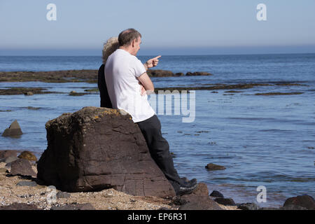 Paar auf Felsen am Meer in der Sonne sitzen Stockfoto