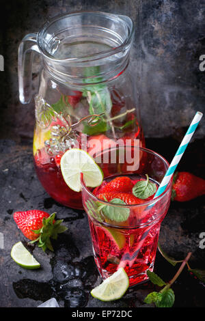 Glas mit Retro-Coctail Röhren und Glaskanne Erdbeer Limonade, serviert mit frischen Erdbeeren, Minze und Limette über dunkle ba Stockfoto