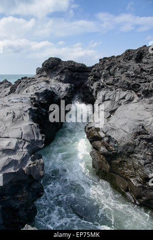 Landschaft mit Spray des Wassers durch schlug Meerwasser durch Tunnel zwischen Felsen an der Küste in der Nähe der Olle Trail Route 16 in Jeju Stockfoto