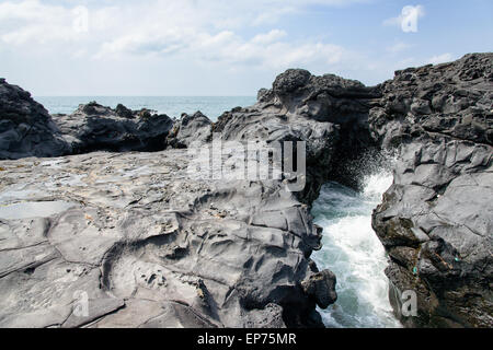 Landschaft mit Spray des Wassers durch schlug Meerwasser durch Tunnel zwischen Felsen an der Küste in der Nähe der Olle Trail Route 16 in Jeju Stockfoto