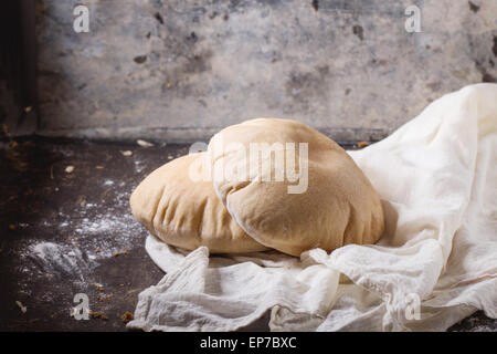 Zwei hausgemachte Vollkorn-Fladenbrot auf weißen Textilien, serviert mit Mehl über dunklen Tisch Stockfoto