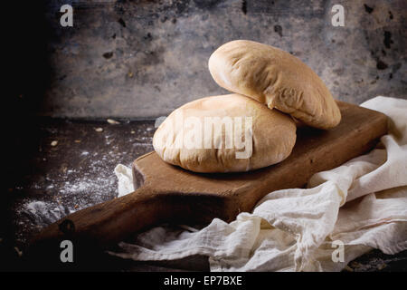 Zwei hausgemachte Vollkorn Fladenbrot auf Holzbrett serviert mit Mehl über dunklen Tisch Stockfoto