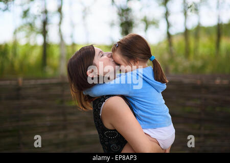 Die Liebe einer Mutter. Mama hält kleine Tochter in die Arme und küßt sie auf die Stirn. Selektiv auf die Gesichter der Modelle. Stockfoto