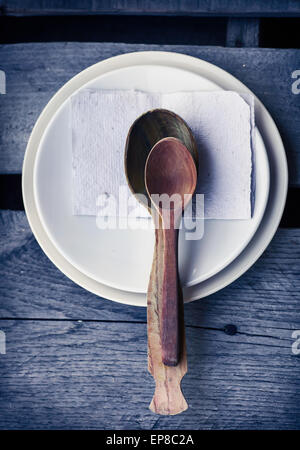 Kochlöffel und weißen Keramikplatten auf alte hölzerne Tabelle Hintergrund, Tisch servieren Stockfoto
