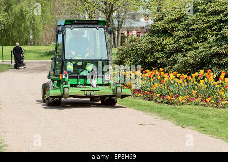 Ronneby, Schweden - 11. Mai 2015: John Deere Rasen schneiden Fahrzeug fährt auf Schotterstraße im öffentlichen Park. Tulpen und Rhododendron wachsen neben Straße. Stockfoto