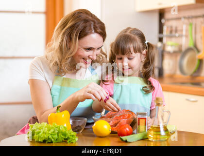 Nette Frau mit Kind Tochter bereitet Fisch in Küche Stockfoto