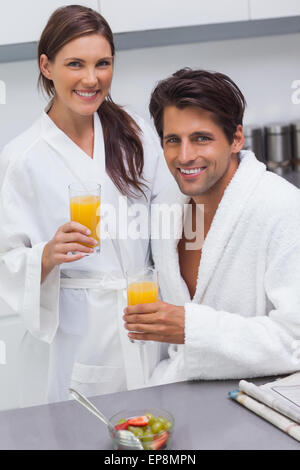 Paar schöne Bademäntel trägt und hält Glas Orangensaft Stockfoto