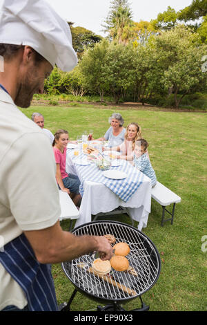 Lächelnd Großfamilie beim Grillen von Vater in Köche Hut gekocht wird Stockfoto