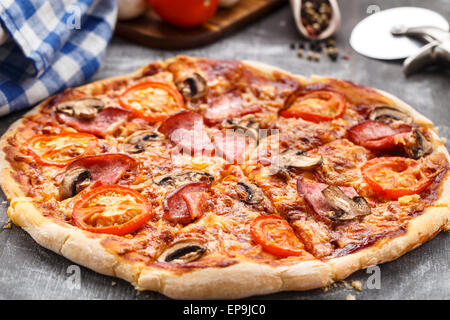 Pizza mit Tomaten, Schinken und Pilzen auf einem Tisch Stockfoto