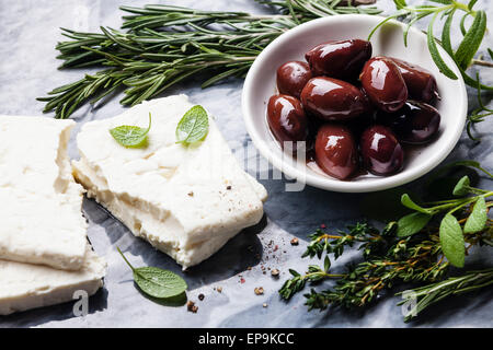 Feta-Käse mit Oliven und grünen Kräutern auf grauem Marmor Hintergrund Stockfoto