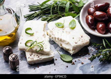 Feta-Käse mit Oliven und grünen Kräutern auf grauem Marmor Hintergrund Stockfoto