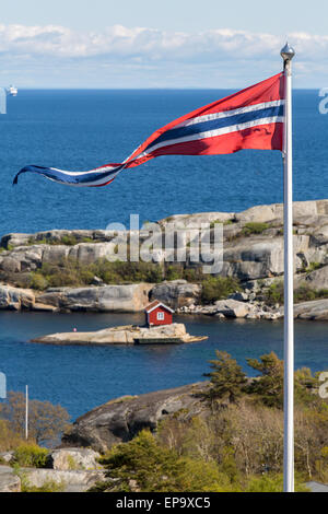 Norwegische Flagge mit einer ziemlich kleinen roten Kabine auf einer winzigen Insel in Norwegen Stockfoto