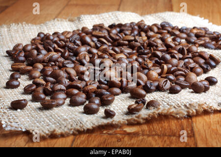 Körner von geröstetem Kaffee auf Leinen Serviette auf Holztisch Stockfoto