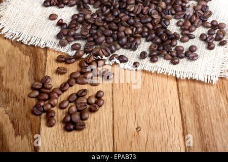 Körner von geröstetem Kaffee auf Leinen Serviette auf Holztisch Stockfoto