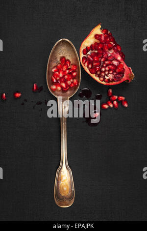 Leckere Reife Granatapfelkerne mit silbernen Löffel auf schwarzem Hintergrund, Ansicht von oben. Gesunde exotische Früchte essen. Stockfoto