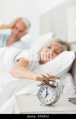 Reife Frau Hand mit Wecker im Bett ausstrecken Stockfoto