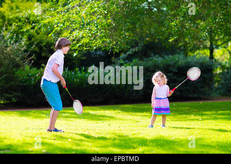 Aktive Kinder Badminton spielen. Zwei glückliche Kinder, die Spaß mit Sport spielen, laufen und springen mit Tennisschläger Stockfoto