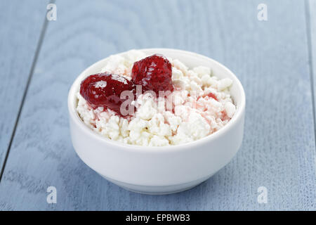 Hüttenkäse mit Erdbeermarmelade in Schüssel weiß auf blau Holztisch Stockfoto