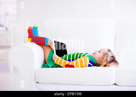 Lustige kleine Kleinkind Mädchen mit Tablet-pc auf einem weißen Sofa entspannen Stockfoto