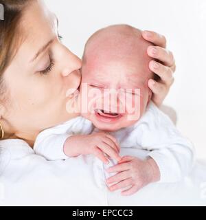 Junge Mutter, die ihr schreiendes neugeborenes Baby küssen Stockfoto