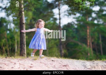 Entzückenden Kind, geschweiften Kleinkind Mädchen in einem blauen Sommerkleid laufen und spielen auf Sanddünen im Pinienwald Stockfoto