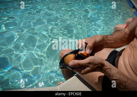 Ein Mann reinigt seine Schwimmbrille, während er am Rand eines Schwimmbades im Pells Pool saß, dem ältesten öffentlichen Süßwasser-Freibad in Großbritannien, in Lewes, East Sussex, England. Stockfoto